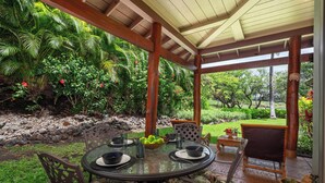 A covered outdoor dining area with a table set for two, surrounded by chairs, and a lush garden backdrop. - Includes Mauna Lani Beach Club. Fairways at Mauna Lani 201 (Mauna Lani Resort)