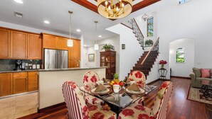 A spacious kitchen with wooden cabinets, a stainless steel refrigerator, and a dining area with floral chairs and a glass table. - Includes Mauna Lani Beach Club. Fairways at Mauna Lani 201 (Mauna Lani Resort)