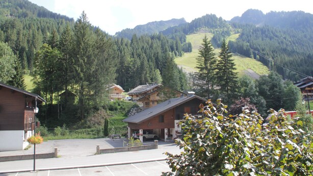 Eine Berghütte mit Parkplatz, umgeben von dichtem Wald und Hügeln.