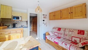 Un espace de vie compact comprenant un coin cuisine, des meubles en bois et un canapé à motifs.