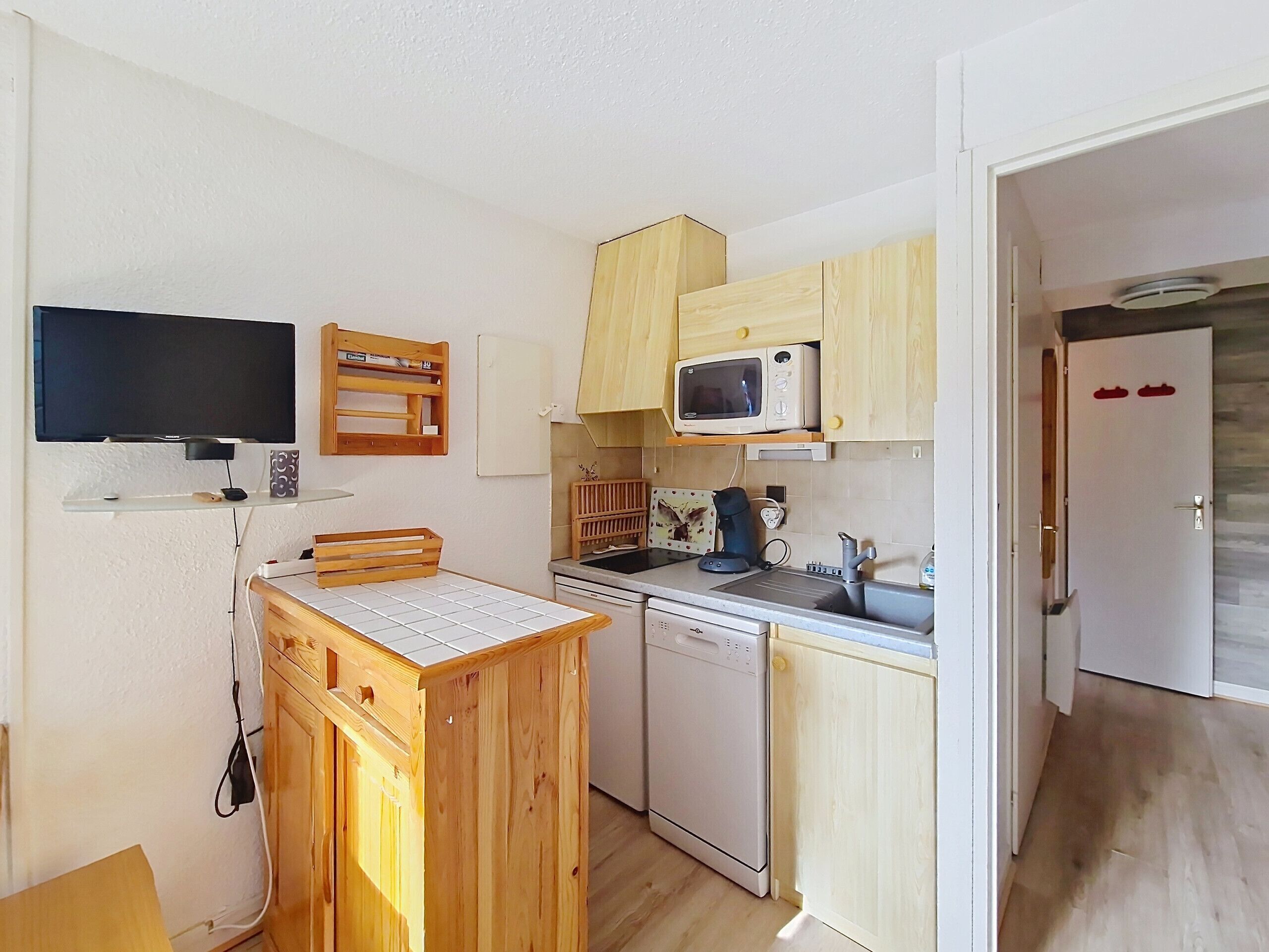 A compact kitchen with wooden cabinets, a microwave, a dishwasher, and a small countertop.
