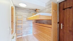 Une pièce avec un lit superposé, des murs en bois, une échelle et une porte.