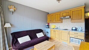 A compact living space with a sofa, a wooden table, and a kitchenette. - SOLARIUM SR19 SUNNY & VIEW 2 Pers. (Châtel)