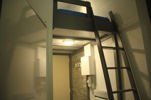 Compact room with a bunk bed and ladder, featuring an area with a window and a functional design.