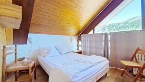 A wooden-paneled bedroom with a bed, two chairs, and a window overlooking a forested area. - Castel des Neiges CSA4 CENTRE & VIEW  6 Pers. (Châtel)