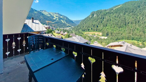 A balcony with a view of a mountainous landscape, a table, and heart-shaped decorations. - Castel des Neiges CSA4 CENTRE & VIEW  6 Pers. (Châtel)