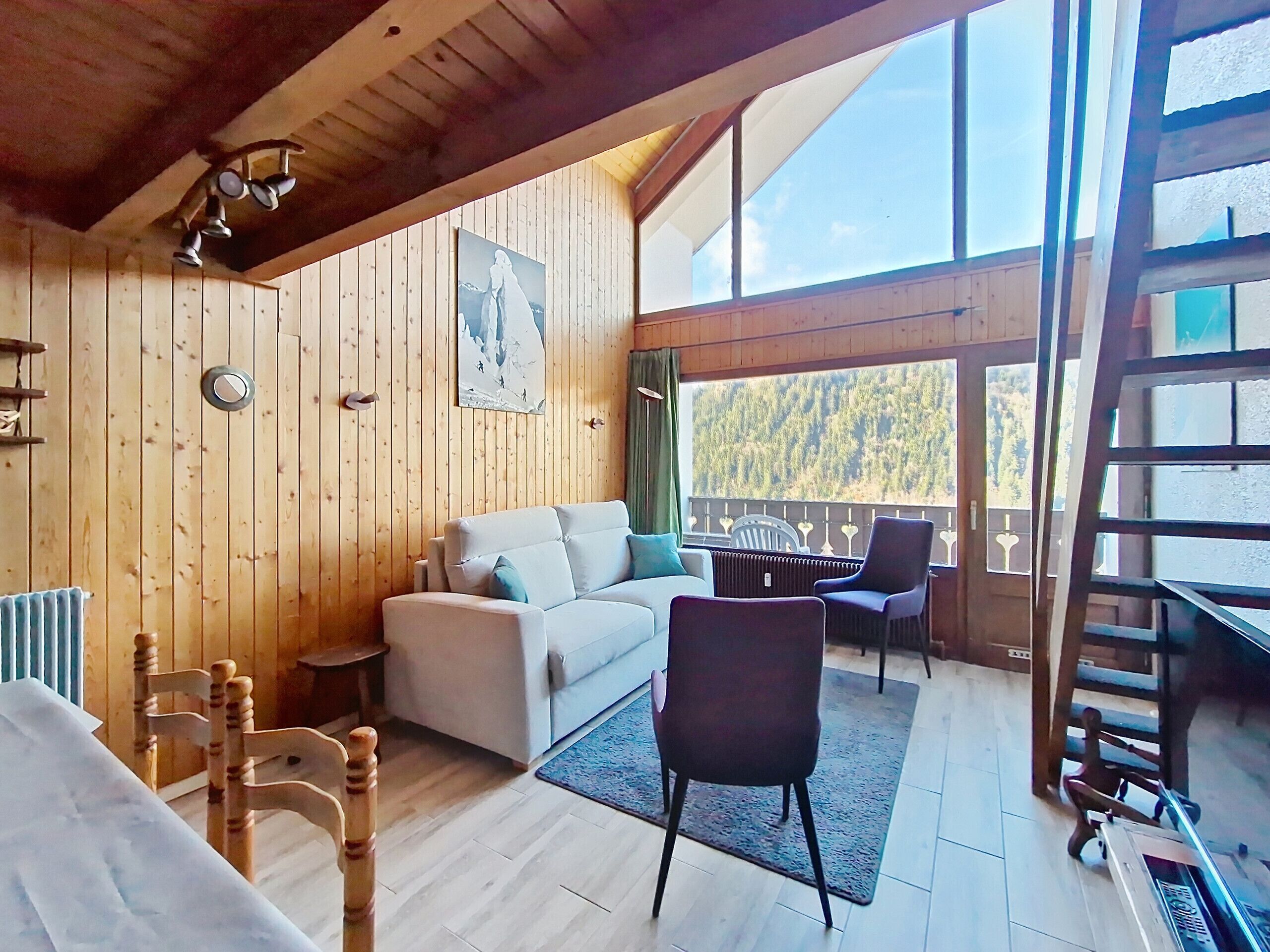 L’intérieur chaleureux d’un chalet en bois comprend un canapé, des fauteuils, une table à manger et une grande fenêtre donnant sur la forêt.
