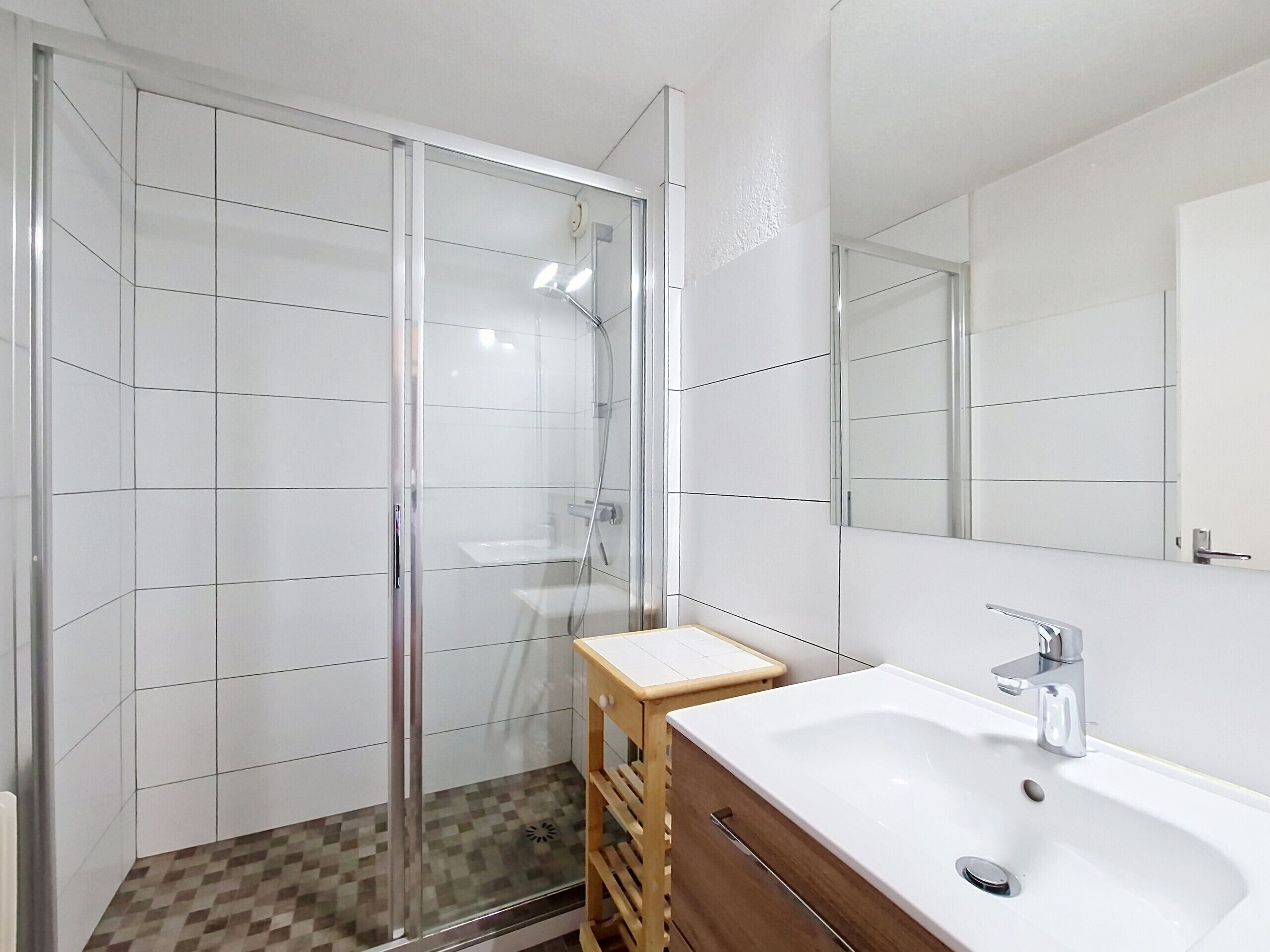 Un baño moderno con ducha envuelta en vidrio, tocador de madera con lavamanos y un espejo grande.