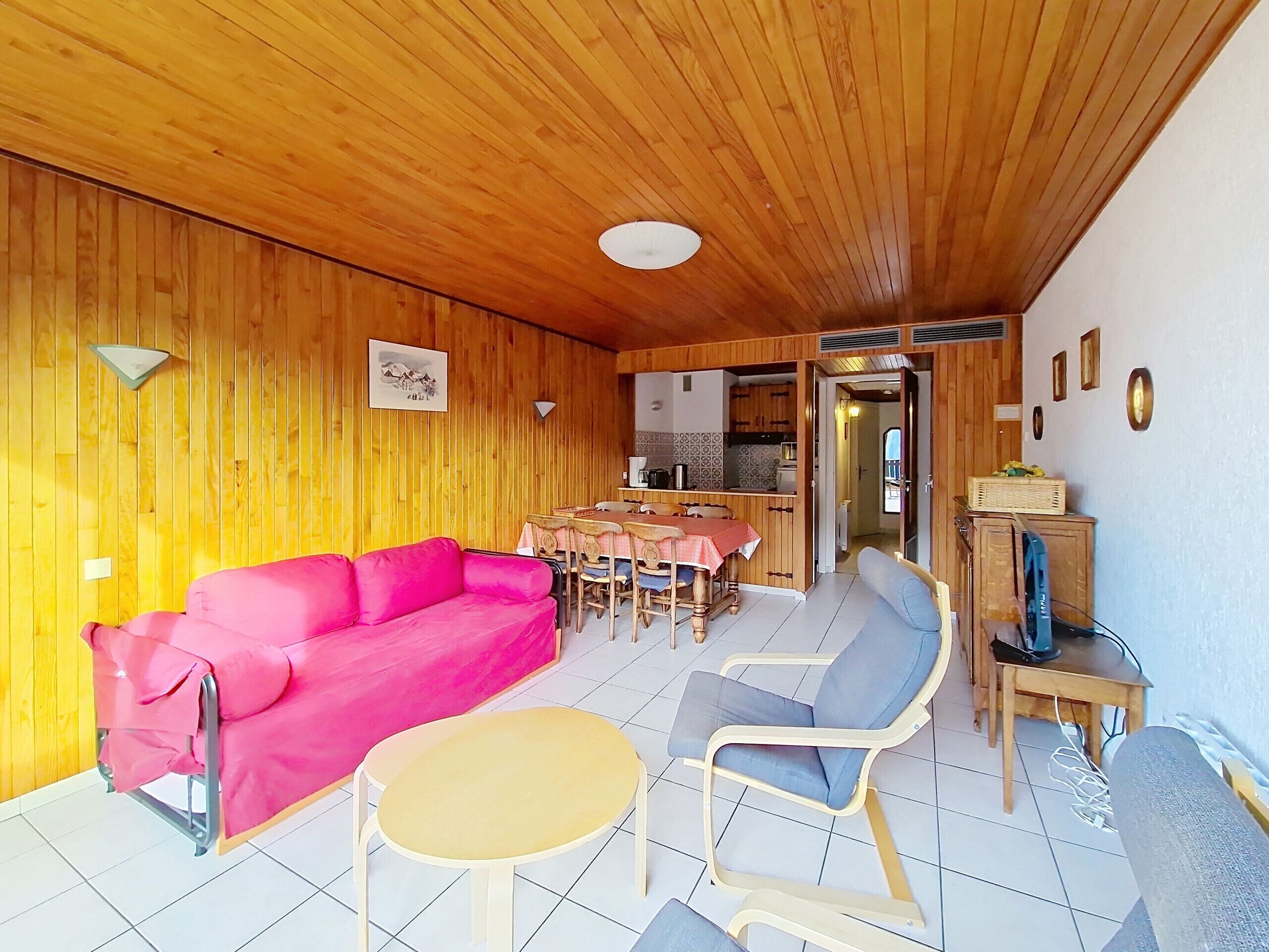 A cozy room with a wooden ceiling, a pink sofa, a small round table, and a blue chair.
