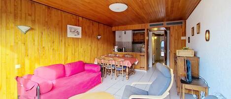 A cozy room with a wooden ceiling, a pink sofa, a small round table, and a blue chair.