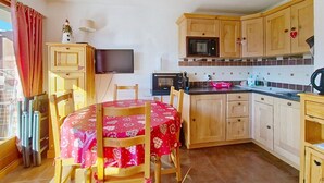 A compact kitchen with wooden cabinets, a microwave, a television, and a dining table with chairs. - Barbessine BBB18 SUN & CHAIR LIFT 4 pers. (Châtel)