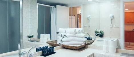 A modern bathroom with a large mirror, two sinks, and a toilet. There are towels and toiletries on the counter.