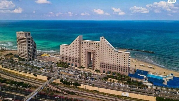 A large hotel with a central courtyard, surrounded by a parking lot and a beach. - Beautiful Apartments by the sea (Haifa)