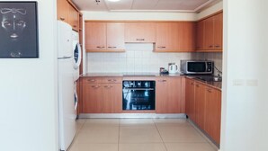 A compact kitchen with wooden cabinets, a built-in dishwasher, a microwave, and a washing machine. - Beautiful Apartments by the sea (Haifa)