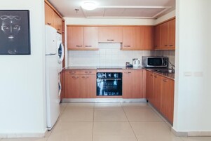 Cocina compacta con armarios de madera, lavavajillas integrado, microondas y lavadora.