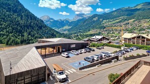 A modern building with a parking lot and a view of a mountainous town. - RESIDENCE RSA18 SWIMMING POOL & CENTER 6 pers. (Châtel)