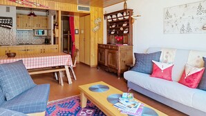 A cozy living room with a sofa, a dining table, and a kitchen area with wooden cabinets and a microwave. - RESIDENCE RSA18 SWIMMING POOL & CENTER 6 pers. (Châtel)