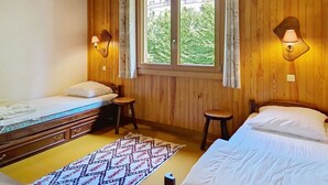 A wooden-paneled room with two beds, a small stool, a nightstand, and a window with curtains. - RESIDENCE RSA18 SWIMMING POOL & CENTER 6 pers. (Châtel)