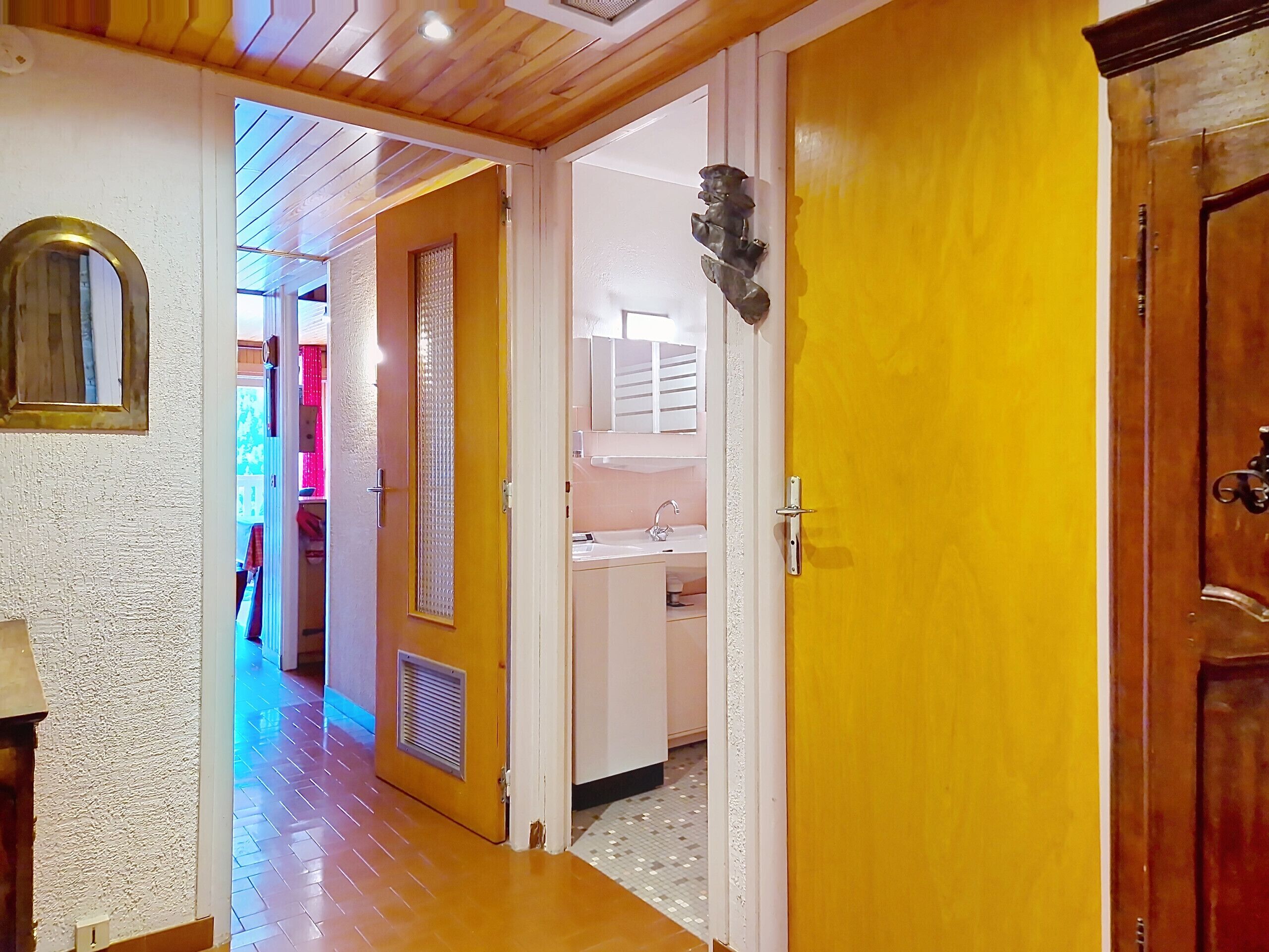 Un pasillo con puerta de madera, pared blanca y suelo de baldosas.
