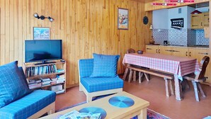 A cozy living room with a TV, bookshelf, blue sofa, and a dining area with a table and chairs. - RESIDENCE RSA18 SWIMMING POOL & CENTER 6 pers. (Châtel)
