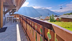 A wooden balcony with a metal railing overlooking a mountainous landscape, a ski lift in the background, and a clear sky. - Chalet Madeline MD25 SUN & VIEW 6 pers. (Châtel)