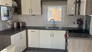A compact kitchen with white cabinets, a built-in microwave, a sink, and a window providing natural light. - Relaxing Lodge In The Heart Of Northumberland (Felton)