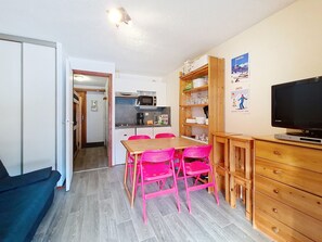 A compact living space with a kitchenette, a dining area with pink chairs, a television, and a wooden cabinet. - Linga LGA101 TELECABINE & NATURE 4 pers. (Châtel)