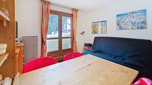Une pièce avec une table en bois, des chaises rouges, un canapé bleu, une fenêtre avec des rideaux et deux tableaux accrochés au mur.