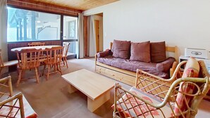 En hyggelig stue med træloft, sofa, sofabord og spiseområde med stole og bord.