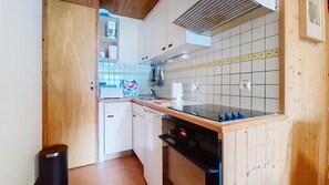 A compact kitchen with white cabinets, a wooden countertop, a black dishwasher, and a tiled backsplash.