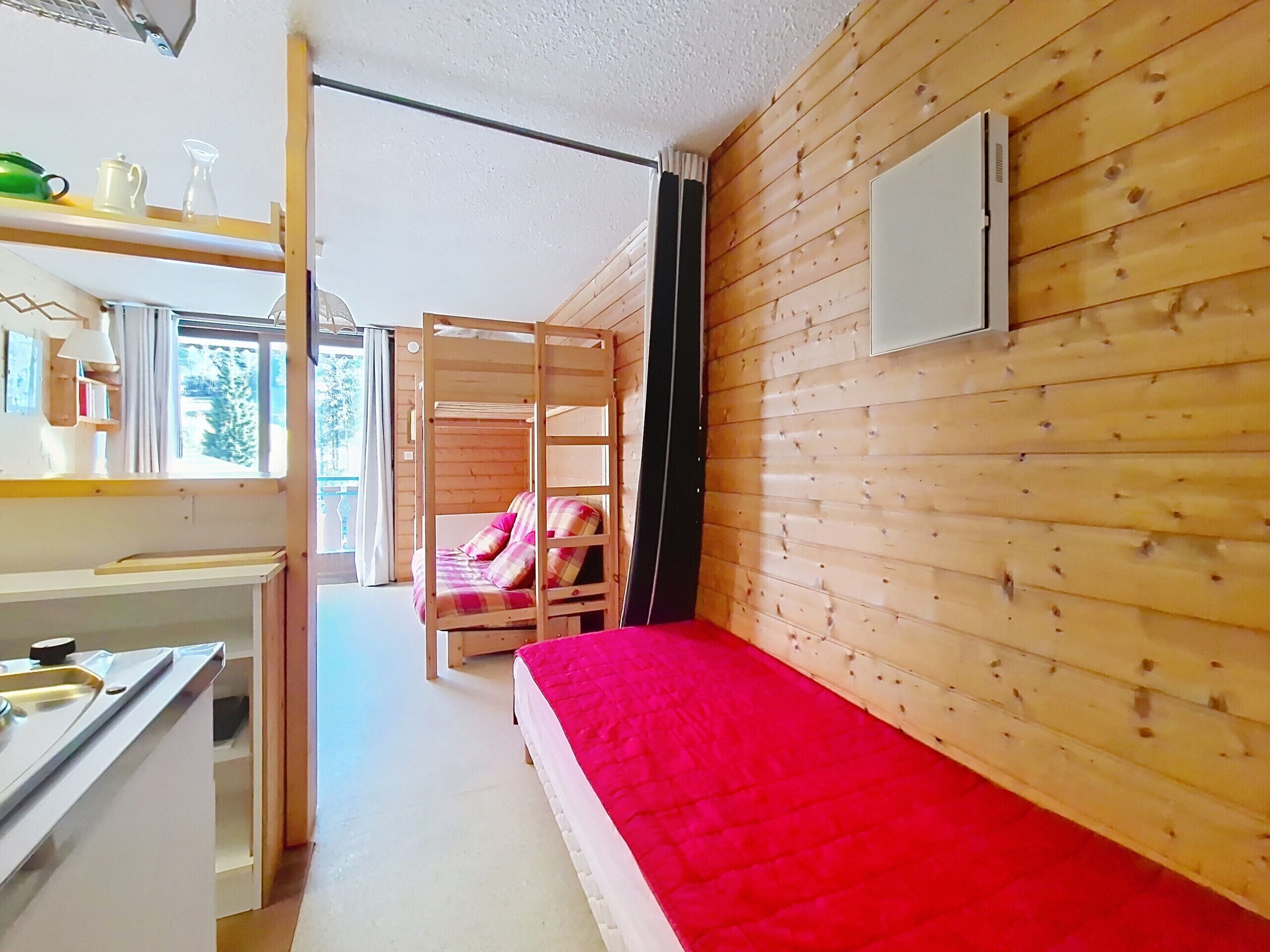 Ein kleines Zimmer mit Etagenbett, einer Küchenzeile und einem fenster mit Vorhängen.