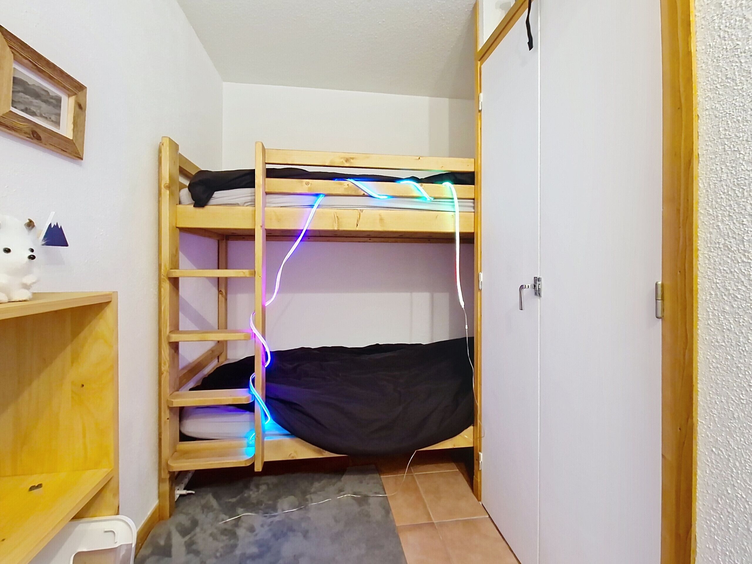 Een kleine, compacte kamer met een stapelbed, een houten plank en een deur.