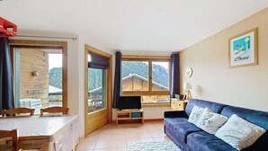 Un salón acogedor con un sofá azul, un televisor sobre un mueble de madera y una mesa de comedor con sillas.