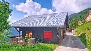 A wooden cabin with a sloped roof, a wooden porch, and a view of a lake and mountains.