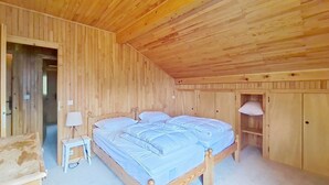 A wooden room with a bed, bedside table, lamp, and wardrobe.