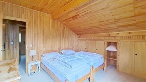 A wooden room with a bed, bedside table, lamp, and wardrobe.