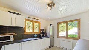 A kitchen with white cabinets, a black countertop, a microwave, a refrigerator, and two windows with wooden frames.