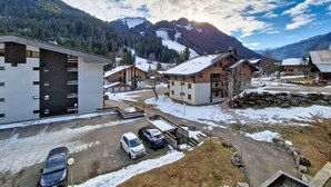 Un pueblo de montaña con casas de madera tradicionales, un edificio moderno y un estacionamiento con automóviles.