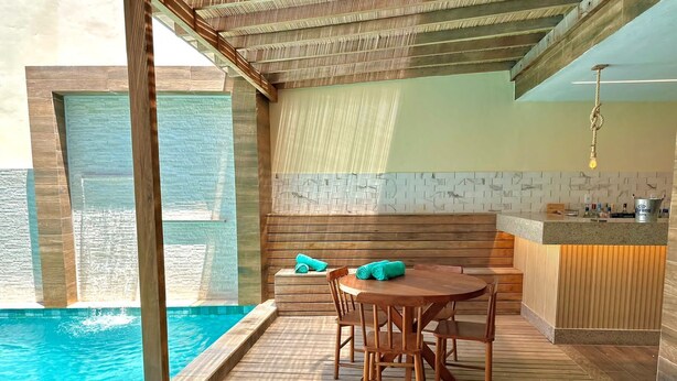 A wooden deck with a pool, a table with chairs, and a bar area. - Humaita Pousada (Itacaré)