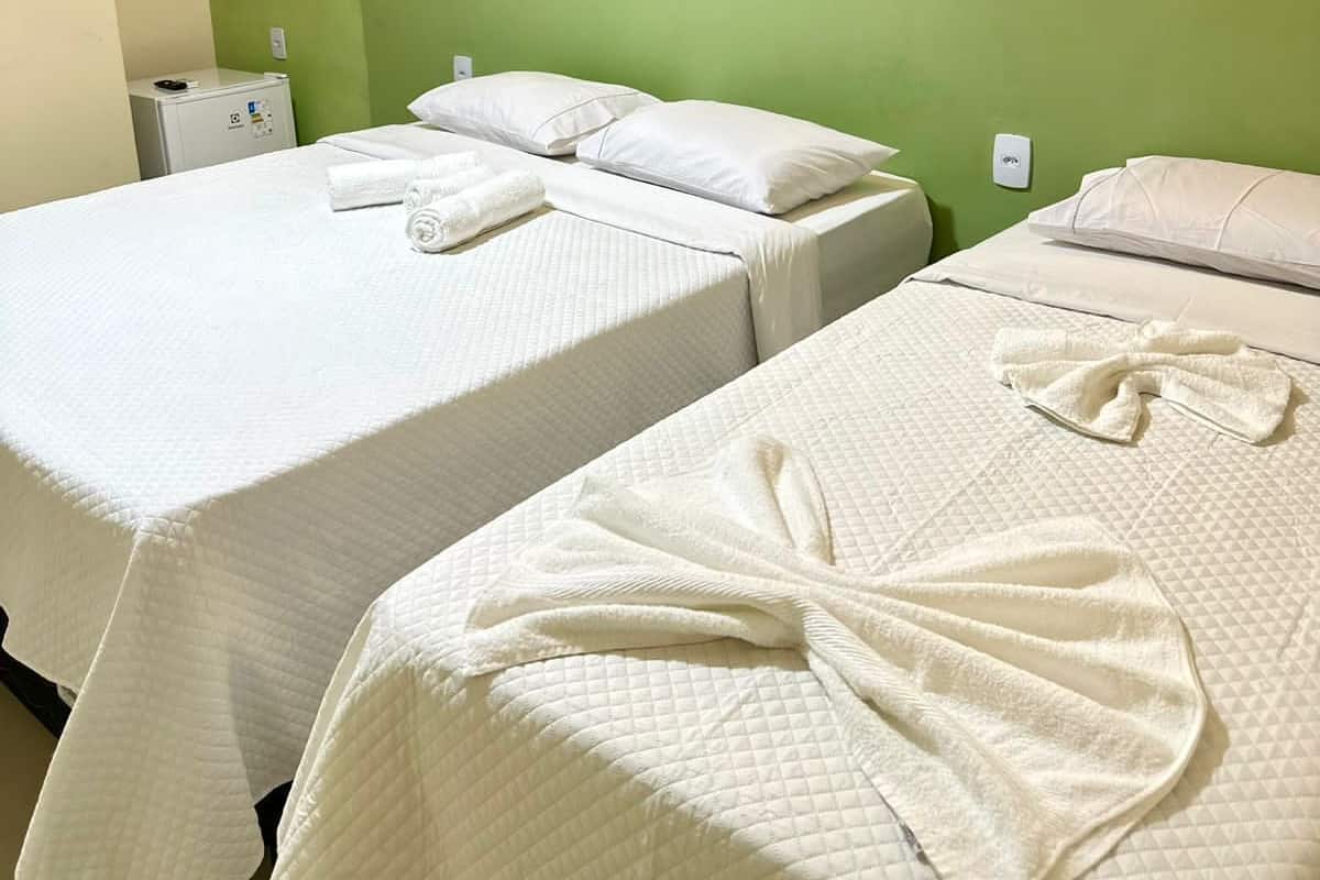 A hotel room with two beds, each with white bedding and pillows, a small heater on the floor, and a green wall.