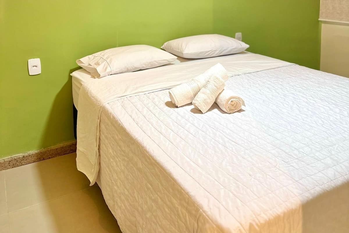 A neatly made bed with white linens and towels, a green wall, and two hanging light fixtures.