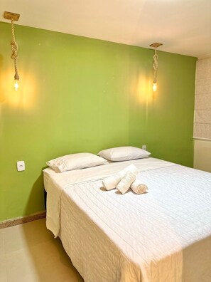 A neatly made bed with white linens and towels, a green wall, and two hanging light fixtures.