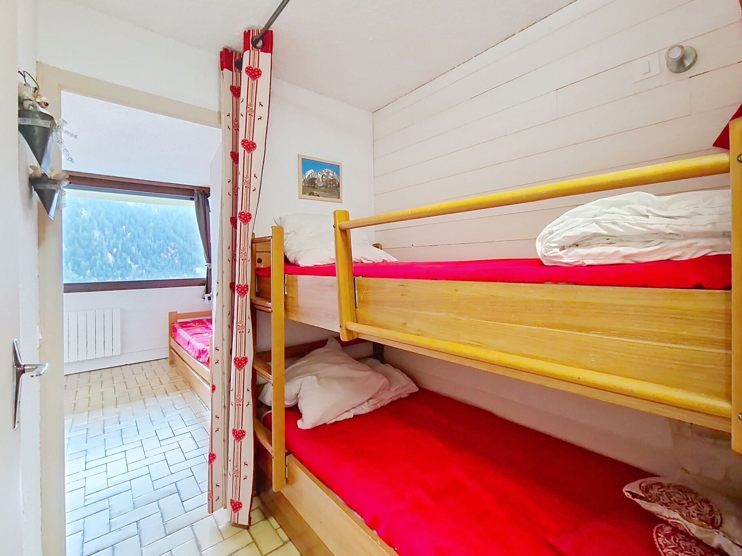 Een slaapzaal met twee stapelbedden, een raam met uitzicht, een radiator en een deur.