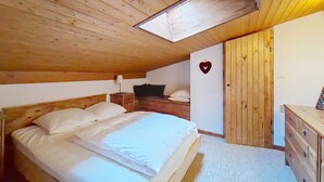 A bedroom with a wooden ceiling, a bed with white linens, a nightstand with a lamp, a dresser, and a heart-shaped decoration on the wall. - Hameau des 4 saisons HSA20  VIEW  & SUN  4 pers. (Châtel)