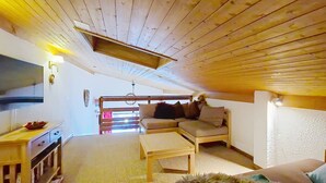 A cozy attic room with a wooden ceiling, a sofa, a small table, and a TV on the left wall. - Hameau des 4 saisons HSA20  VIEW  & SUN  4 pers. (Châtel)