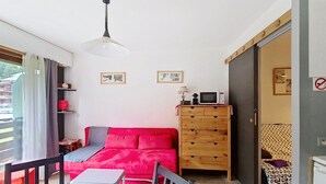 Un espacio habitable pequeño con un sofá rojo, un aparador de madera, una mesita y un microondas en un estante.