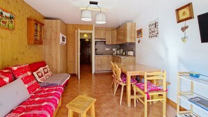 Un salón acogedor con un sofá rojo, una mesa de comedor de madera y sillas. Se ve una cocina al fondo con armarios de madera y un microondas.