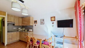 Una cocina compacta con armarios de madera, una mesa de comedor con sillas, un televisor y una cortina roja.