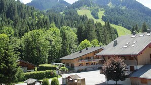A lodge with a mountain backdrop, featuring a parking area and a building with a sloped roof. - Portes Du Soleil PSB204 TELECABINE & MOUNTAIN 4 pe (Châtel)