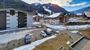 A mountain village with modern and traditional buildings, a parking area, and a view of snow-capped mountains. - Portes Du Soleil PSA46 TELECABINE & MOUNTAIN 4 Per (Châtel)